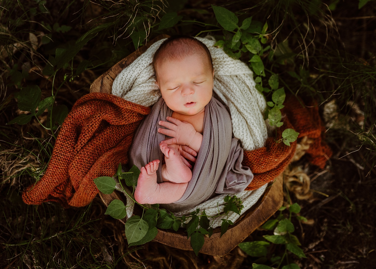 sleeping newborn baby wrapped in blankets in woodland setting
